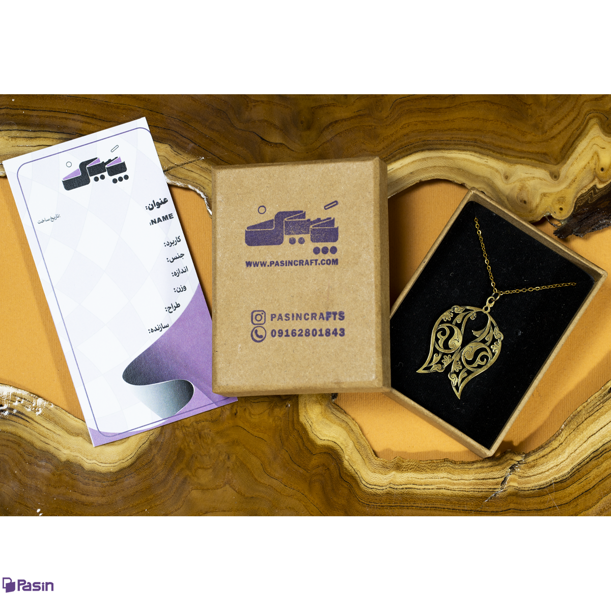 گردن‌آویز برنجی طرح اسلیمی بادامی همراه با بسته بندی و شناسنامه که در فضای بین، طرح نبودن یک ماهی را نمایش داداه است.